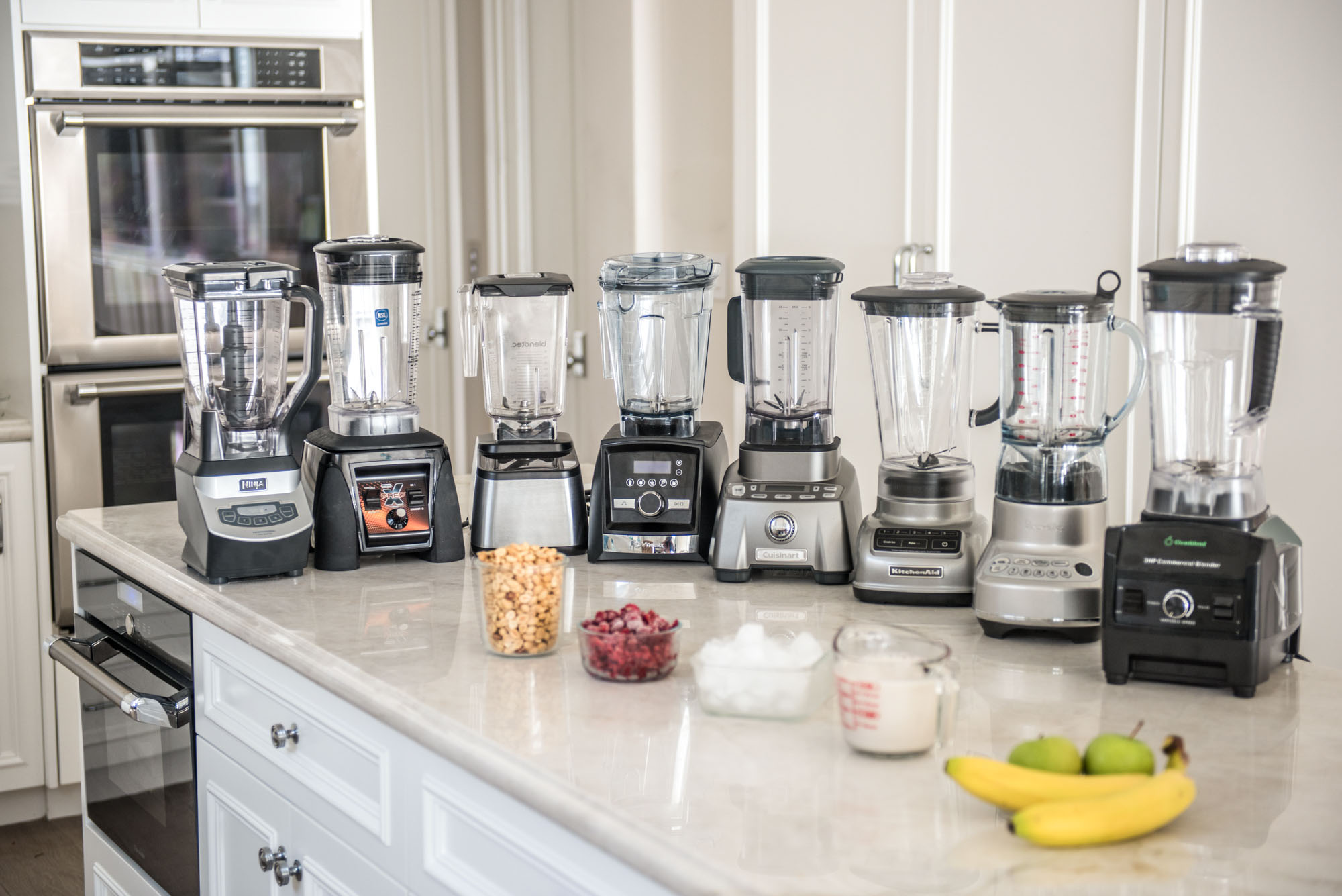 Blenders lined up with ingredients on a counter.